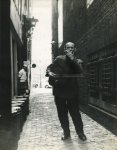 SIEBEN, J. - Straatmuzikant met gitaar en mondharmonica in een Amsterdamse steeg in de nabijheid van het Damra, 10 October 1962.