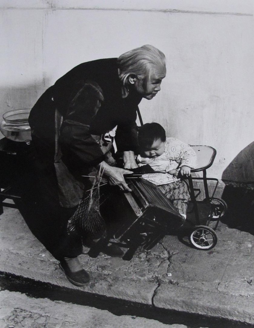HANSEN, Ben - China. Chinese grandmother with grandchild in the street with all kinds of attributes.