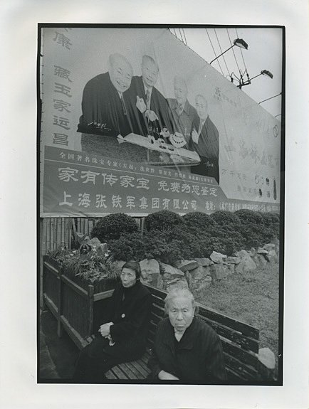 SHANGHAI. - Two older women on a wooden bench in front of an ideological poster with smiling men of importancy.